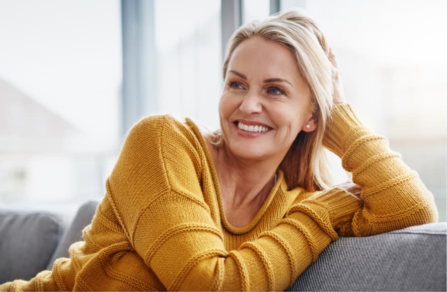 A woman wearing an orange sweater, sitting on a couch, and smiling.