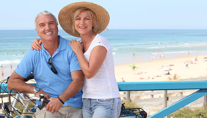 Man and woman sitting on a bicycle smiling with the beach in the background