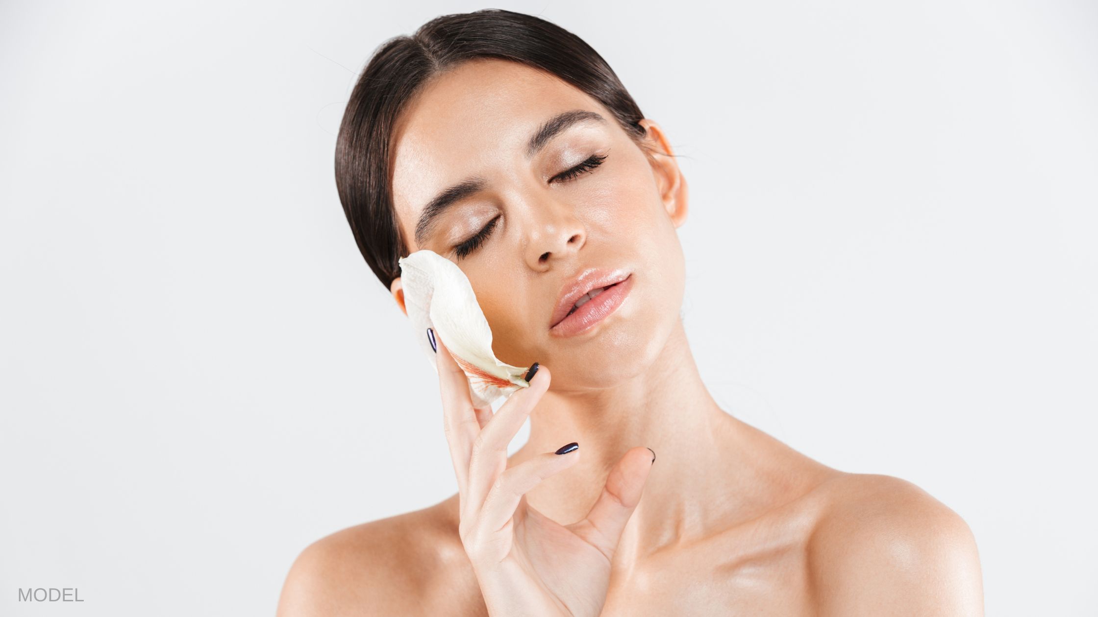 Woman with eyes closed holding a flower petal to her face. (MODEL)