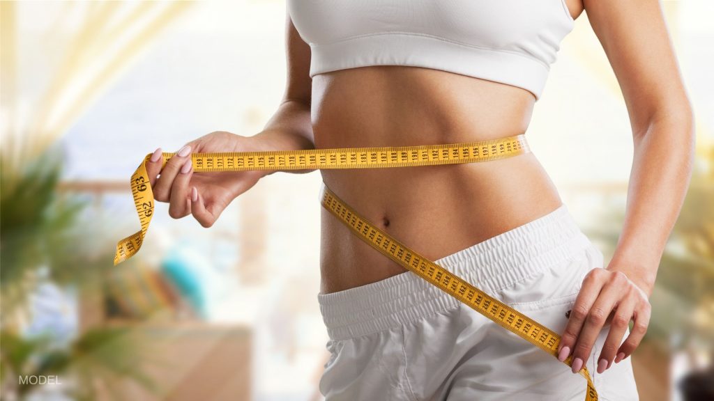 A woman's flat stomach with a measuring tape wrapped around it. (MODEL)